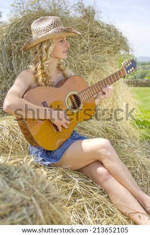 Sexy cowgirl playing on guitar, sitting on hay.