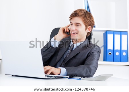 businessman talking on mobile phone using laptop, happy smile sitting at the desk in office talking cellphone, handsome young business man phone call, looking at computer screen