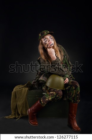 army girl, soldier woman sitting hold helmet wear military camouflage uniform cap, full length portrait over black background