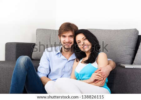 young couple sitting on floor near sofa happy smile looking at camera, portrait of lovely young man and woman hug, embrace on the couch in living room