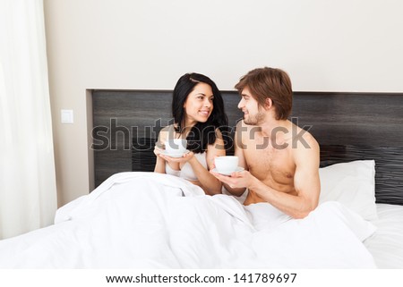 young couple drink coffee in bed, happy smile woman man looking to each other lovers, love romantic valentine day morning talk concept