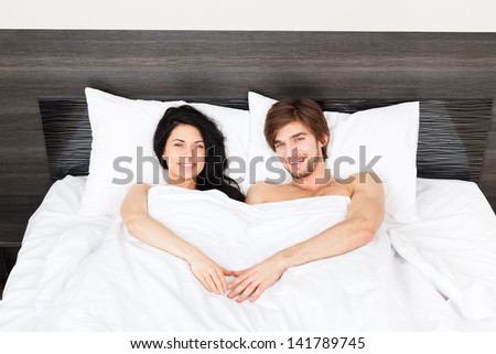 young couple lying in a bed, happy smile man and woman lovers in bedroom, hold hands heart shape valentine day concept
