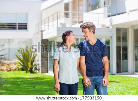 Happy couple family near new house, man and woman outdoor holding hands looking to each other smile concept of real estate