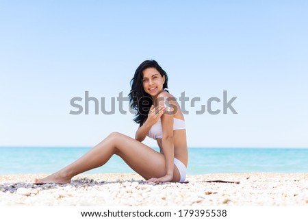 woman apply sunscreen protection lotion hand on arm shoulder, young girl smile with tanned body, sitting on summer beach travel ocean vacation, female applying suntan cream skin care sun protect
