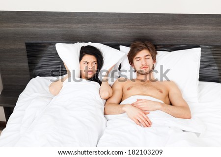 Couple in bed, snoring man. woman can not sleep, covering ears with pillow for snore noise, sleeping in bedroom at home