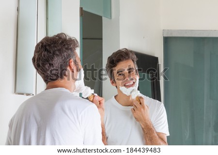 man shaving his face happy smile at home bathroom, looking mirror