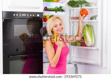 pretty girl hold red yellow pepper, near refrigerator open door, diet healthy food concept, young woman smile vitamin vegetables