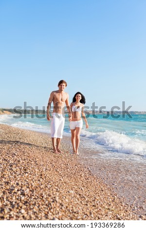 Couple walking on beach, love hold hands. Young happy man and woman walk sea shore romantic smiling, summer ocean vacation holiday blue sky