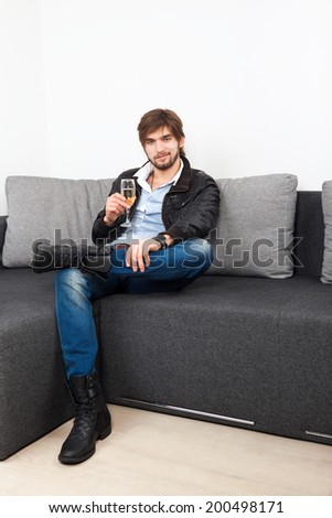 man glass of champagne sitting on sofa living room, fashion macho guy hipster wear boots leather jacket