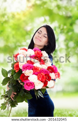 beautiful woman with big roses bouquet smile smell with closed eyes, elegant dress over green tree park outdoor background, concept of 8 march holiday or valentine\'s day