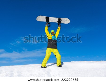 Snowboarder raised hands arms up hold snowboard on top of hill, snow mountains snowboarding on slopes