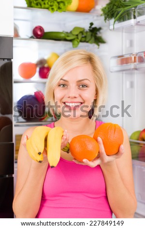 young woman hold banana orange in hands near open door refrigerator, concept of diet health food, pretty girl hold vitamin fruit