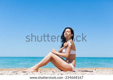 woman apply sunscreen protection lotion hand on arm shoulder, young girl smile with tanned body, sitting on summer beach travel ocean vacation, female applying suntan cream skin care sun protect