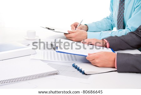 Two business people in elegant suits sitting at desk working in team together with documents sign up contract, holding clipboard, folder with papers, business plan. Isolated over white background.