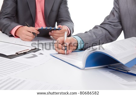 Two business people in elegant suits sitting at desk working in team together with documents sign up contract, holding clipboard, folder with papers, business plan. Isolated over white background.
