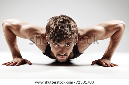 Sexy Young fashion sport man, fitness muscle model guy making push ups exercise over gray background.