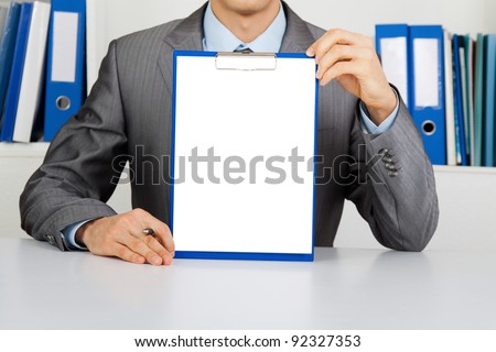 businessman holding a blank white board, signboard, clipboard with paper, showing an empty bill board with copy space for text, unrecognizable person sitting at the desk at office