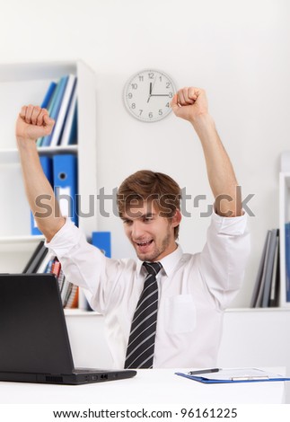 Successful excited young business man happy smile sitting at the desk hold raised arms hand up using computer, handsome businessman working on laptop, using computer, concept of success, victory, win