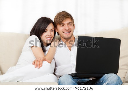 beautiful young couple sitting on a sofa happy smile, using laptop, portrait of lovely young man and woman hug, embrace on the couch