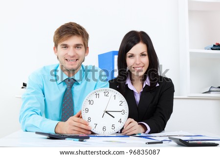 Business people hold clock, Businessman and businesswoman sitting at the desk in office, happy smile