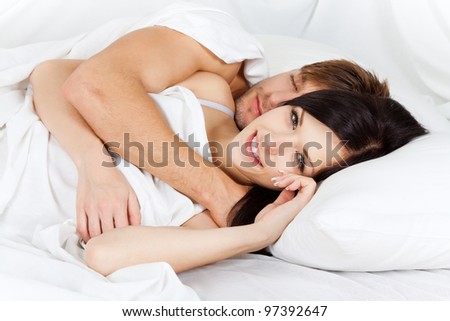young lovely couple lying in a bed, happy smile woman looking at camera, man sleep with closed eyes