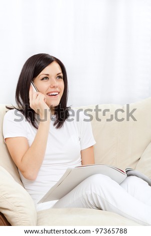Young happy smile woman phone call read magazine on sofa in living room,  at home - indoors, sitting talking using cellphone on chair