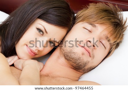 young lovely couple lying in a bed, happy smile woman looking at camera, man sleep with closed eyes, close up view.