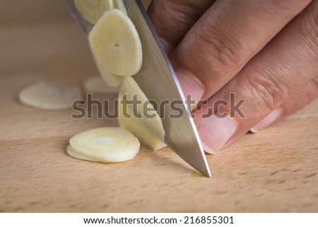 Chef slicing garlic cloves on the cutting board with a knife