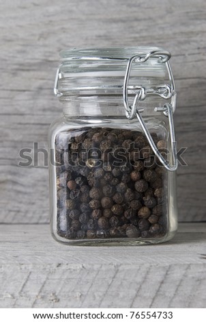 A jar with black peppercorns on an old wooden stand.