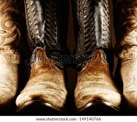 High contrast photo of several pair of worn cowboy boots, with center pair being a matched pair.