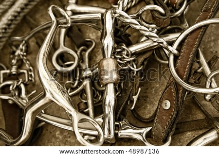 Sepia tinted close-up of a pile of well-used horse bits, tack leather and a rope (shallow depth of field).