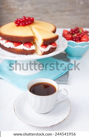 Coffee with Victoria sponge cake with buttercream frosting, jam and strawberries on the stand with cut slice, selective focus