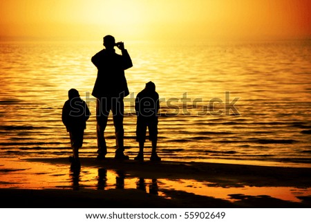 Silhouettes of father and two sons by the ocean looking to the sunset