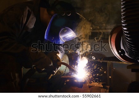 Welder working with welding helmet, sparks and smoke around him