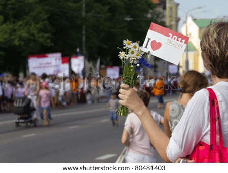 TALLINN, ESTONIA - JULY 3: Woman watch the parade of the 11th Youth Song and Dance Celebration in Tallinn. Estonia, on July 3, 2011, and hold the flag of Culture Capital Tallinn 2011.