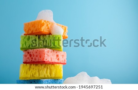 Household Cleaning Scrub Colored Sponges with soap foam. Kitchen Dishwashing Sponge on blue background. Cleaning home concept. Space for text.