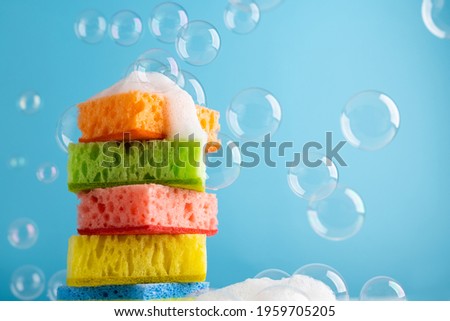 Household Cleaning Scrub Colored Sponges with soap foam and bubbles. Kitchen Dishwashing Sponge on blue background. Cleaning home concept. Space for text.