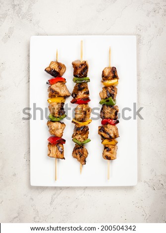 Grilled meat and vegetable kebabs on the white plate.