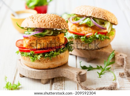 Fish and crab burgers with fresh vegetables on wooden serving boards