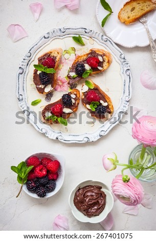 Sweet berry bruschetta with chocolate nut butter,mint and sliced almonds on the white vintage dish