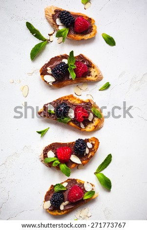 Sweet berry bruschetta with chocolate nut butter,mint and sliced almonds on the white vintage dish