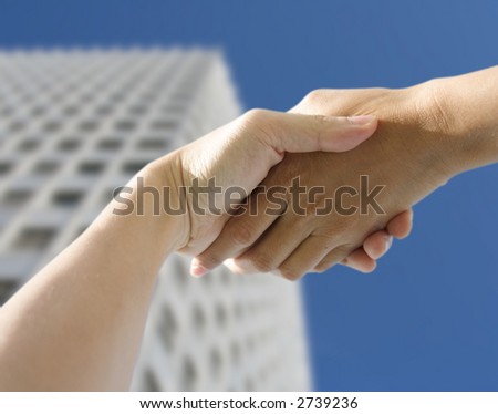 A pair of hands holding or shaking each other against a building background. Concept: Business deal done.