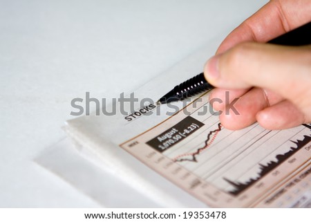 Hand holding pen on a financial newspaper.