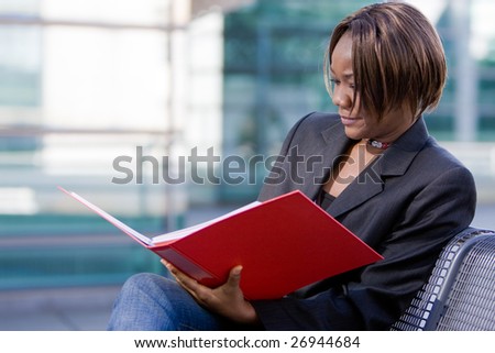 African american business woman reading documents in a folder in front of an office building