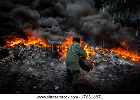 Grandpa throws a tire into the fire, to defend against attack police. Ukraine, Kiev (01.23.2014)