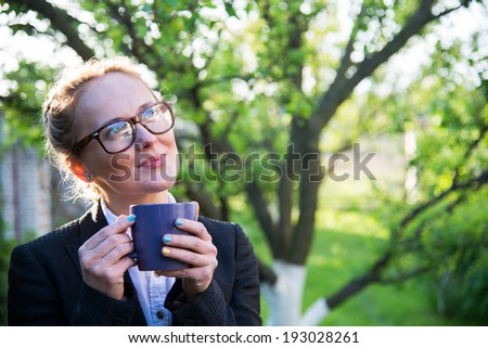 Girl in glasses holding a blue cup in hands.  Girl looks into the distance.