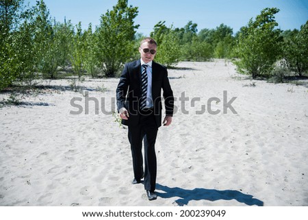 A man in a business suit in sunglasses walking on sand