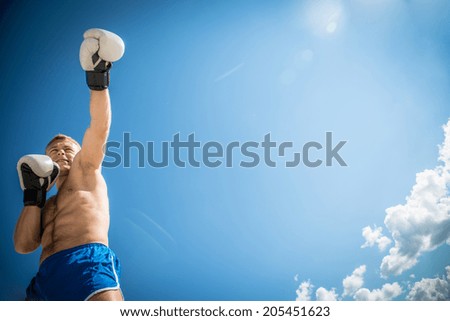 Athletic guy in blue shorts and boxing gloves fulfills kick exercising in nature