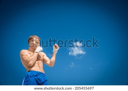 Athletic guy in blue shorts and boxing bandages fulfills kick exercising in nature