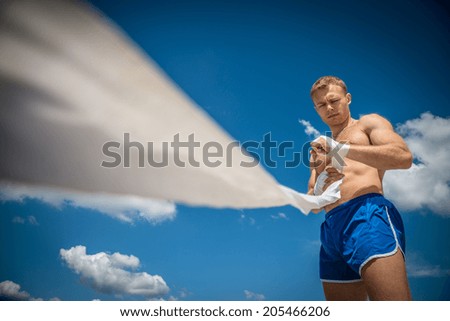 Athletic guy in blue shorts pulls on hand boxing bandages